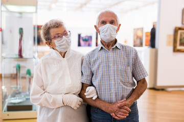 Fototapeta premium mature couple in mask protecting against covid examines paintings on display in hall of art museum