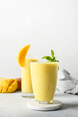 Two mango lassi in glasses on gray background. Indian healthy vegan beverage with mango. Freshness...