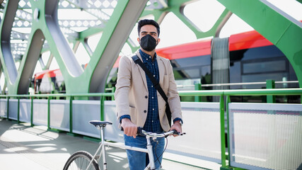 Fototapeta na wymiar Young business man commuter with bicycle going to work outdoors on bridge in city, coronavirus concept.