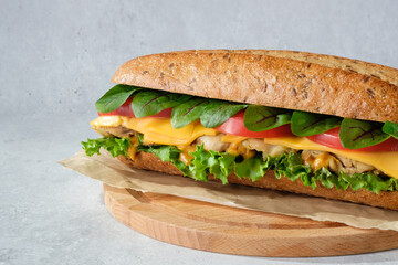 Sandwich with lettuce, tomatoes, chicken, cheese and sorrel close-up on wooden cutting board.
