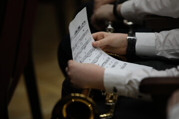 A sheet of music in the hands of a schoolboy in a white shirt sitting with a musical instrument...
