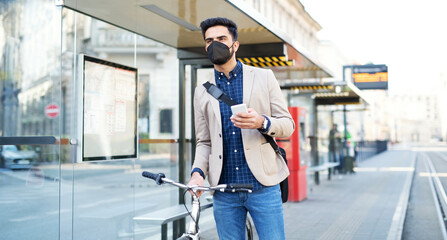 Young business man commuter with smartphone on the way to work outdoors in city, coronavirus...