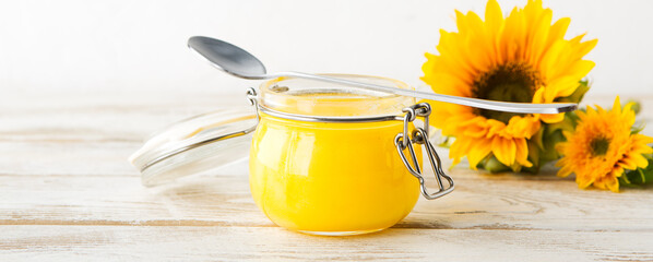 ghee in a glass jar and sunflowers on a light background, shallow depth of field, space for text