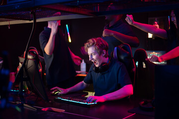 Two guys and a girl in medical masks in a computer club give support to their friend during his game