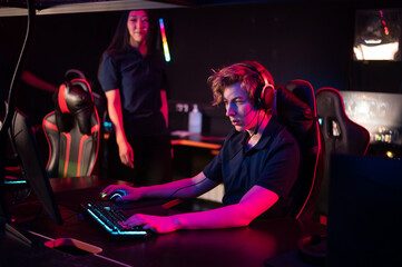 A young asian girl flirts with a guy in a computer club, she smiles and offers help in the game