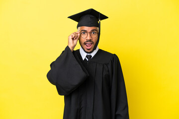 Young university graduate Colombian man isolated on yellow background with glasses and surprised