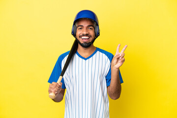 Young Colombian latin man playing baseball isolated on yellow background smiling and showing...