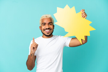 Young Colombian handsome man isolated on blue background holding an empty speech bubble with surprised expression