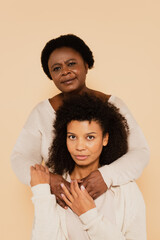 Obraz premium portrait of african american middle aged mother and adult daughter hugging and holding hands isolated on beige