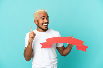 Young Colombian handsome man isolated on blue background holding an empty placard and thinking