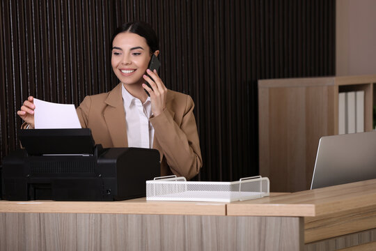 Receptionist talking on smartphone at countertop in office - Powered by Adobe