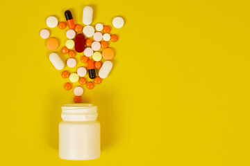 A white bottle with scattered multicolored pills on a yellow background. The concept of the impact of vitamins on human life
