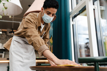 Young waiter disinfecting table in cafe