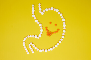 A cheerful face in a stomach of pills shows its tongue on a yellow background. Healthy eating show tongue to poor digestion tongue