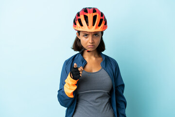 Young cyclist woman isolated on blue background frustrated and pointing to the front - obrazy, fototapety, plakaty