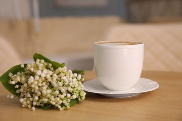 Cup of aromatic morning coffee and flowers on wooden table in cafe