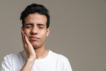 Brunette hispanic man with toothache frowning and rubbing his cheek