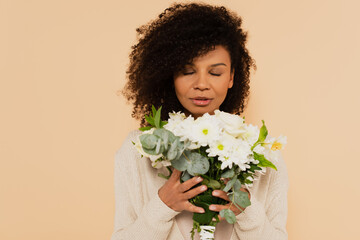 african american woman smelling bouquet of daisies with closed eyes isolated on beige