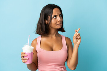 Young woman with strawberry milkshake isolated on blue background with fingers crossing and wishing the best