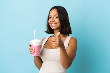Young woman with strawberry milkshake isolated on blue background with thumbs up because something good has happened