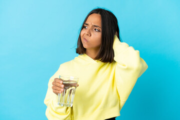 Young asiatic woman with a glass of water isolated on blue background having doubts