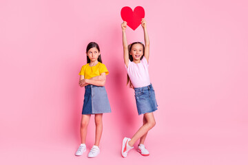 Full length body size view of attractive cheerful girls holding heart card isolated over pink pastel color background
