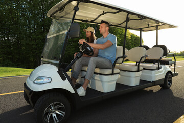 Happy couple driving golf cart on road in park