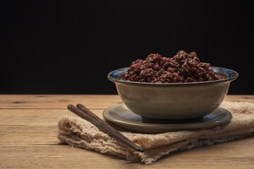 Cook Ripe Berry Rice in a bowl with wooden chopsticks on wood table with a black background. Brown rice, Black Jasmine rice.