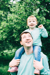 daughter sits on her father's neck in a green park. international day of men. father's day. great...