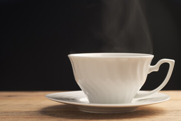White cup of hot coffee or tea with smoke on wooden table with a black background. Fresh tasty espresso cup of hot coffee.