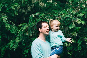 daughter sits with father in her arms in a green spring park. international day of men. father's...
