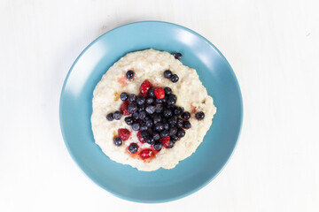 Oatmeal with honey, blueberries and strawberries in blue plate on white background