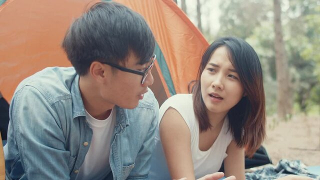 Young asia campers couple laying in tent in forest. Male and female traveler relaxing and talking on a summer day at campsite. Outdoor activity, adventure travel, or holiday vacation.