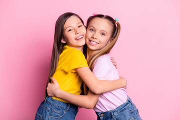 Portrait of two charming kind cheerful girls wearing casual hugging good mood isolated over pink pastel color background