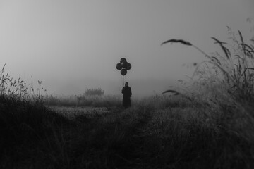 man in a costume of a terrible monster in a Cape with a hood stands in the fog in a field