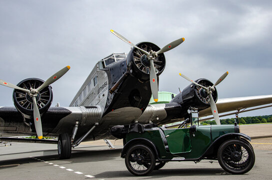 The historical plane "Tante Ju" Junkers Ju 52 on a cloudy day with an Austin oldtimer on the apron in front of the engines