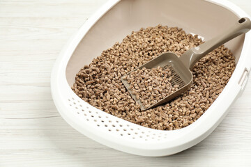 Cat litter tray with filler and scoop on white wooden floor, closeup