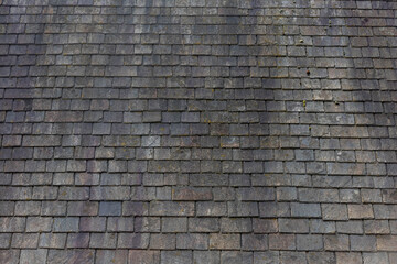 Old dark brown stone tiles covered with moss and rust stain on brick roof, Shingles texture,...