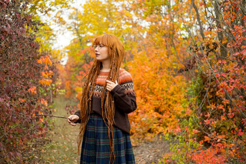 Young woman with red dreadlocks and wearing a sweater in the beautiful autumn forest