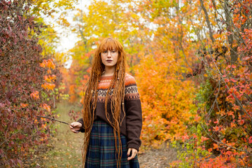 Fototapeta na wymiar Young woman with red dreadlocks and wearing a sweater in the beautiful autumn forest