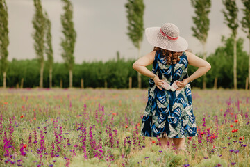 Back view of happy mom holding her future baby shoes, standing in field, carrying a hat and enjoying the warm weather