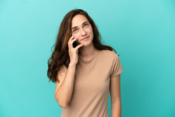 Fototapeta premium Young caucasian woman isolated on blue background keeping a conversation with the mobile phone with someone