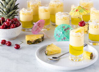 A close up of a pineapple jelly parfait on a round ceramic platter with other parfaits and ingredients in behind.