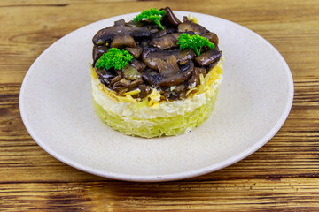 Tasty layered salad with roasted mushrooms, potato, eggs, cheese and mayonnaise on wooden table