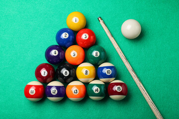 Set of billiard balls and cue on green table, flat lay