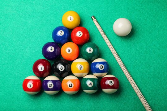 Set of billiard balls and cue on green table, flat lay
