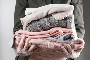Feminine hands wear disposable vinyl gloves holding neatly folded pile of warm clothes. Donation,...