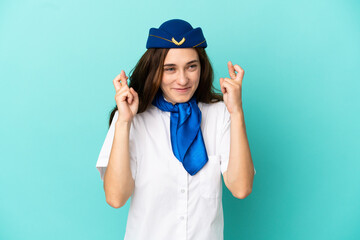 Airplane stewardess woman isolated on blue background with fingers crossing