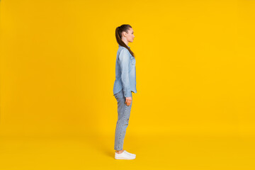 Fototapeta na wymiar Full length photo of sweet charming young lady dressed jeans shirt standing looking empty space smiling isolated yellow color background