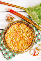 Above view of homemade round baked rhubarb ( Rheum hybridum ) pie white rustic wood table background. Rhubarb stalks on side. Seasonal spring dessert.